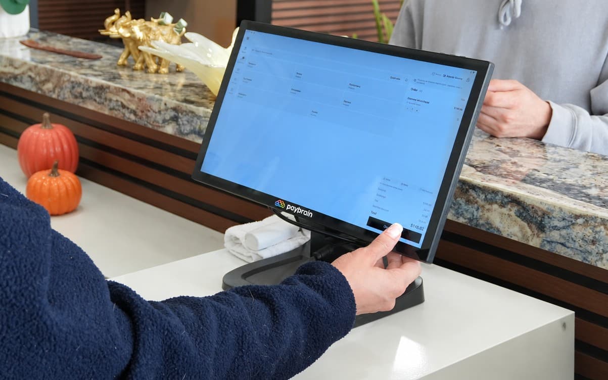 At a spa front desk, the register rings up a member's facial with the member discount already applied while the client waits across the counter