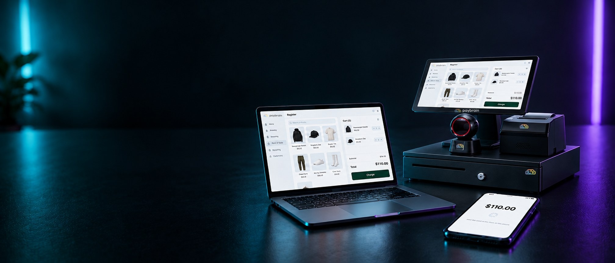 On a dark table, the Paybrain Register kit, a laptop running the Paybrain web register and a phone waiting for a Tap to Pay card, all showing the same $110.00 sale